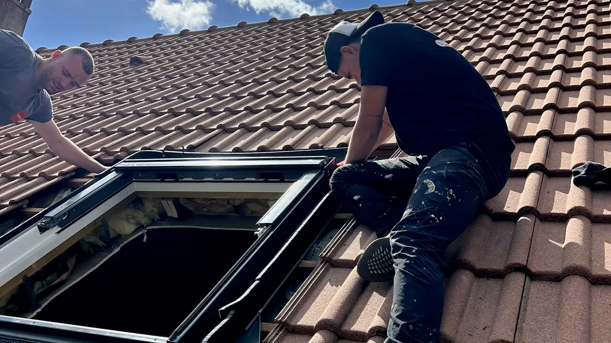Deux couvreurs installent une fenêtre de toit Velux sur une toiture en tuiles